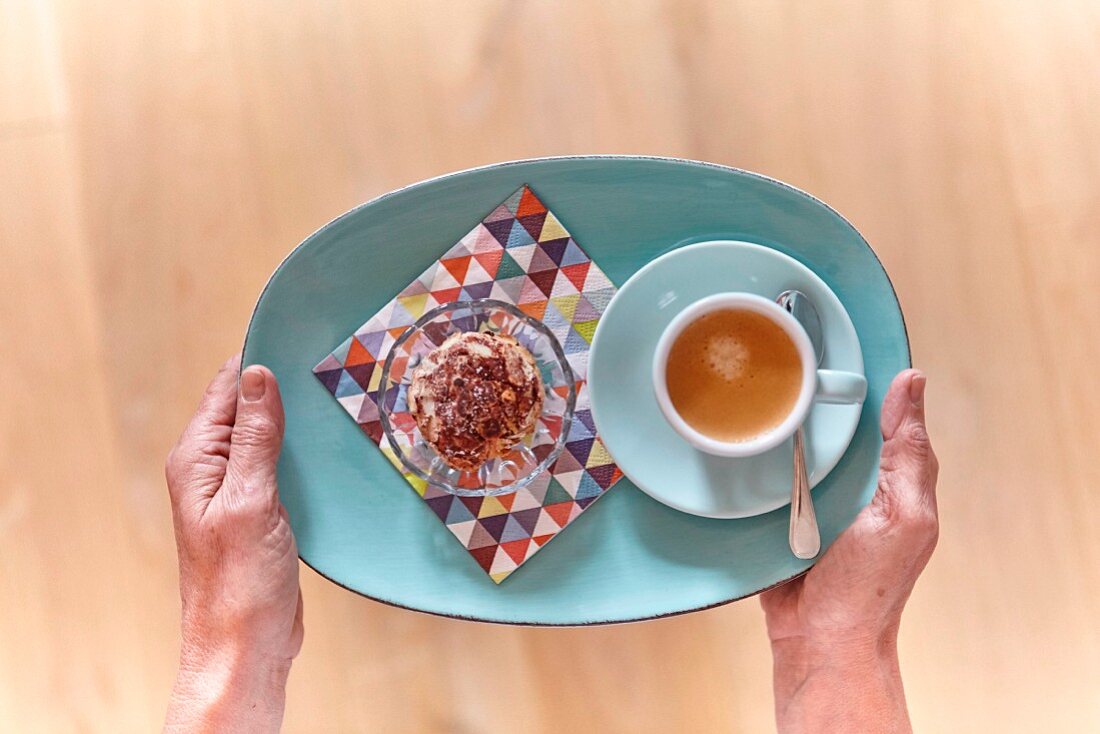 Frauenhände halten einen Teller mit Dessert und einer Tasse Espresso