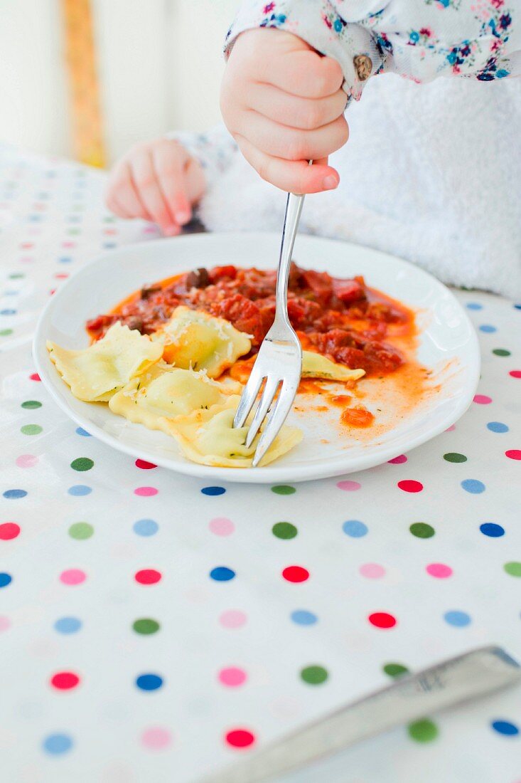 Kind sitzt am Tisch und isst Ravioli mit Sauce