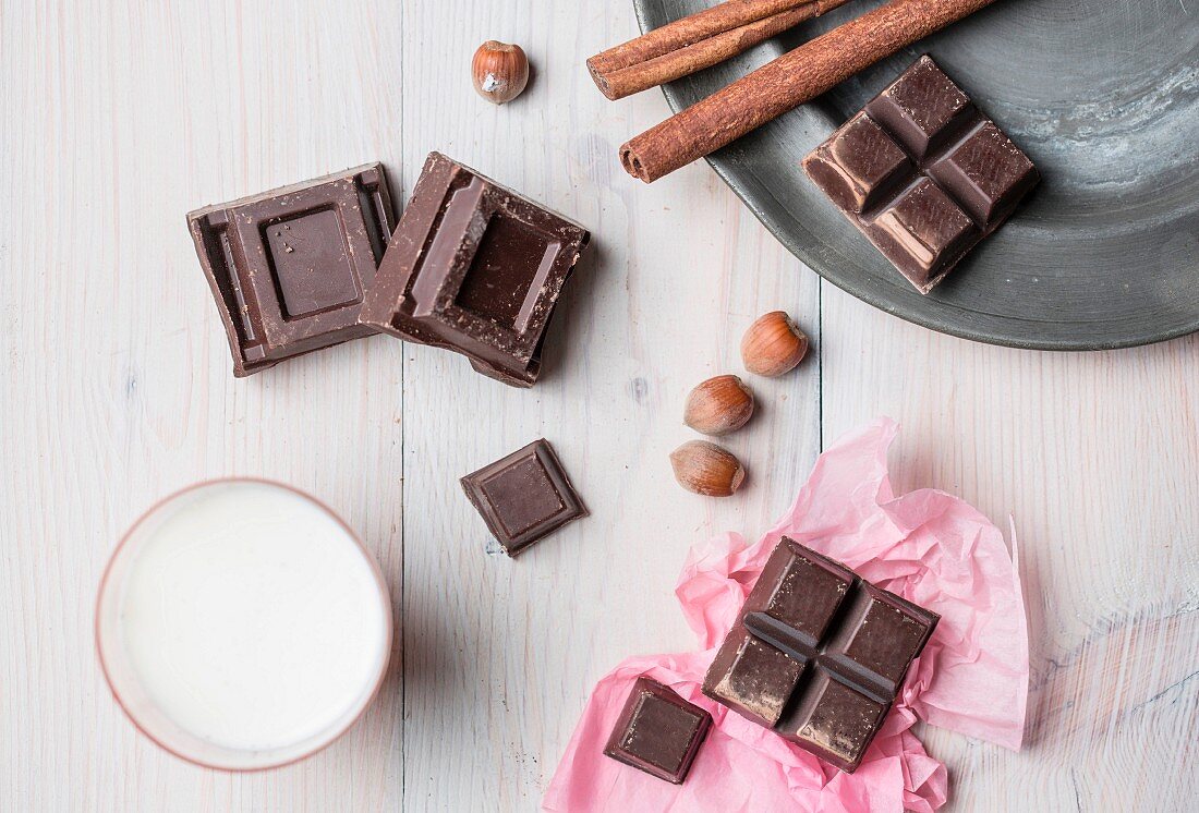 An arrangement featuring chocolate pieces, cinnamon, nuts and a glass of milk (seen from above)