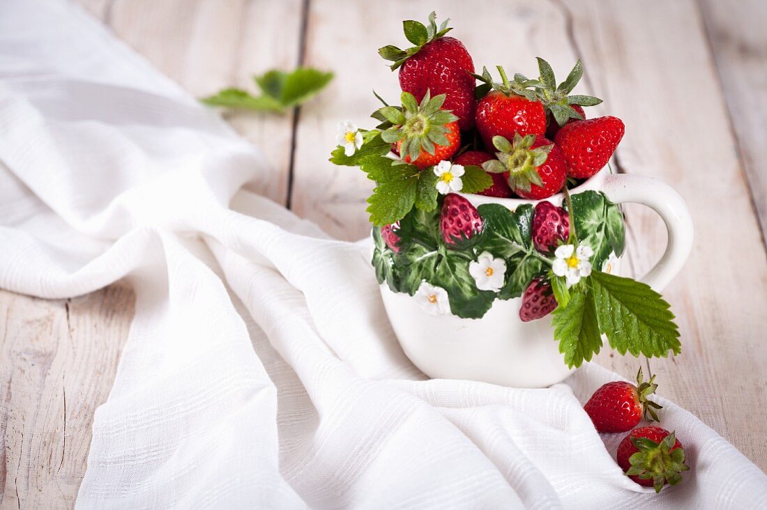 Erdbeeren mit Blättern und Blüten in Keramiktasse