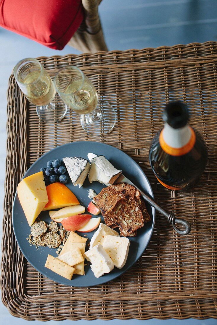 A cheese platter and champagne on a wicker table