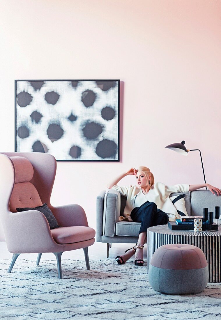Frau auf grauem Sofa neben rosa Ohrensessel und Sitzpouf