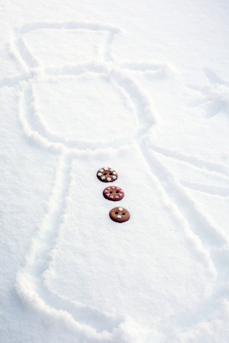 Schneemann in Schnee gezeichnet mit Knöpfen aus Lebkuchenteig