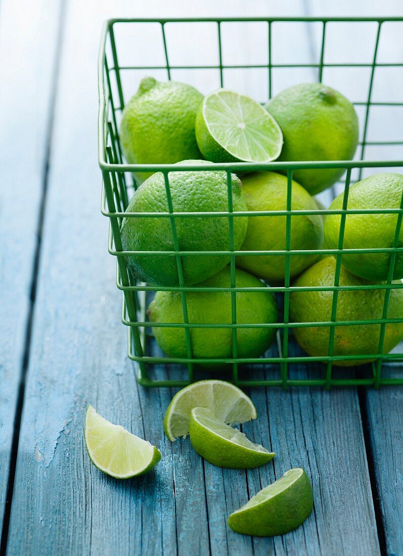 Limes in a green wire basket with lemon wedges in the foreground