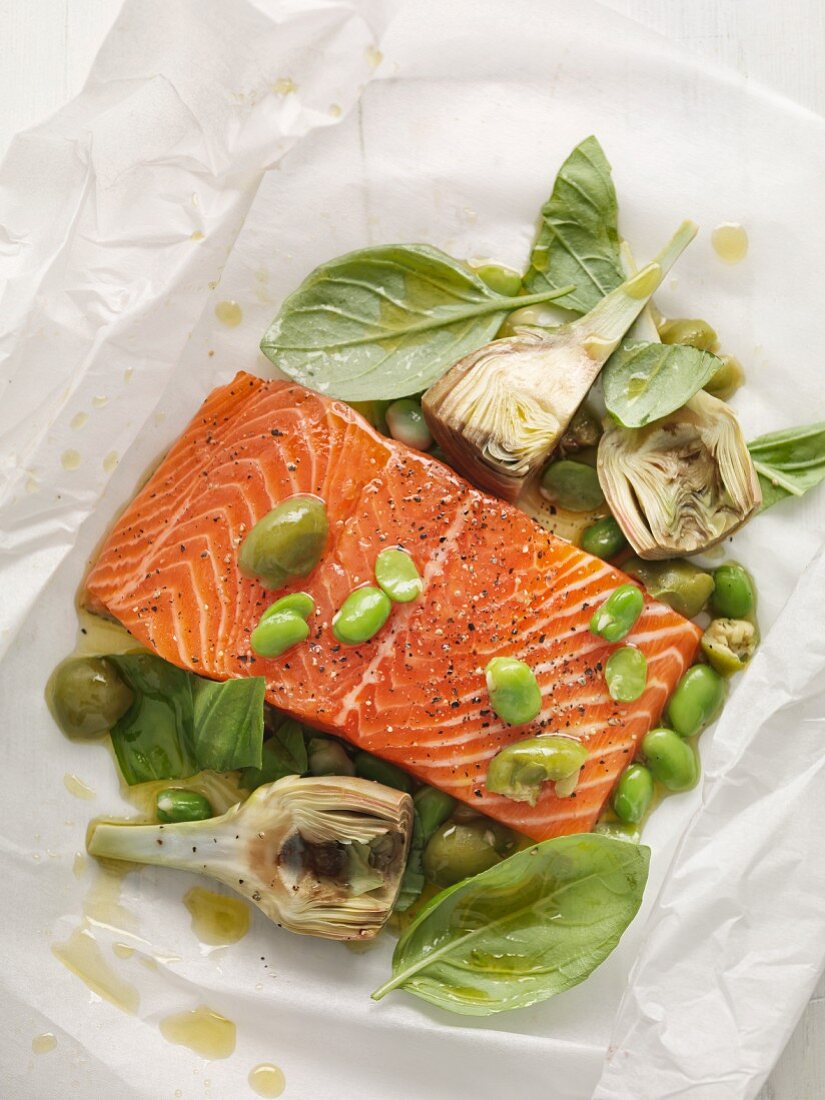 Seasoned salmon fillet with olives and artichokes on parchment paper