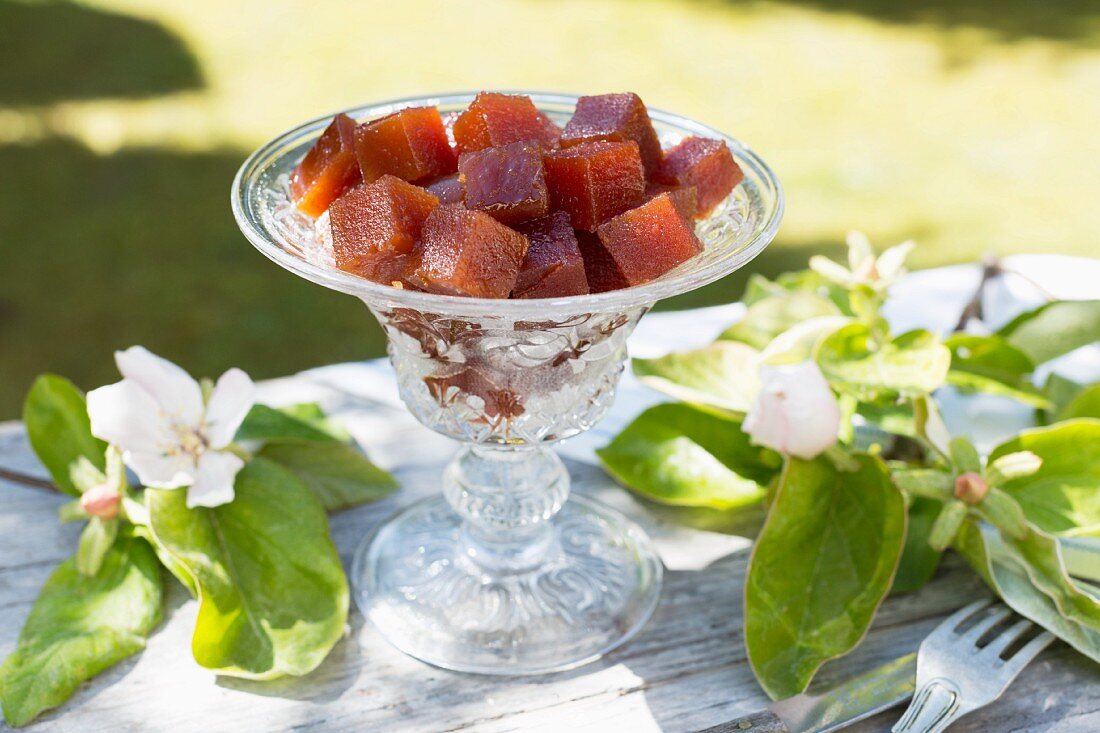 Quince jelly cubes in an old glass bowl on a table outdoors, with quince flowers and branches