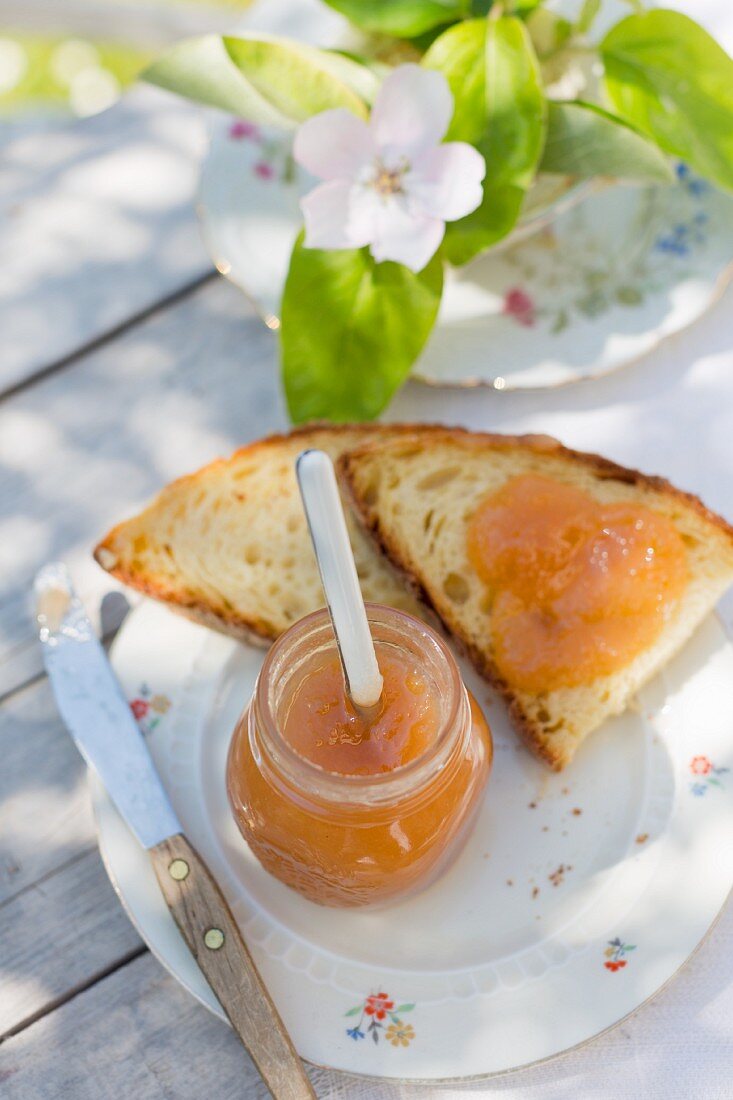An outdoor breakfast with quince marmalade in a jar and on white bread, with quince flowers and branches