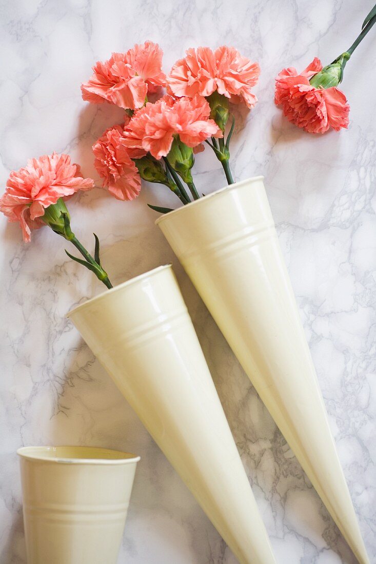 Salmon-pink carnations in conical metal vases on marble surface