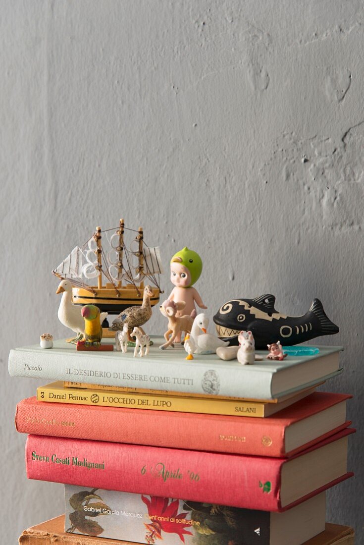 Retro-Spielzeugfiguren und Miniaturen auf Bücherstapel vor grauer Wand