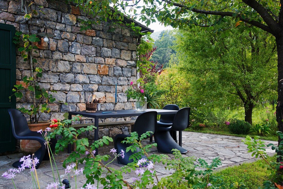 Rustico mit Terrassenplatz und schwarzen Klassiker-Schalenstühlen um Tisch