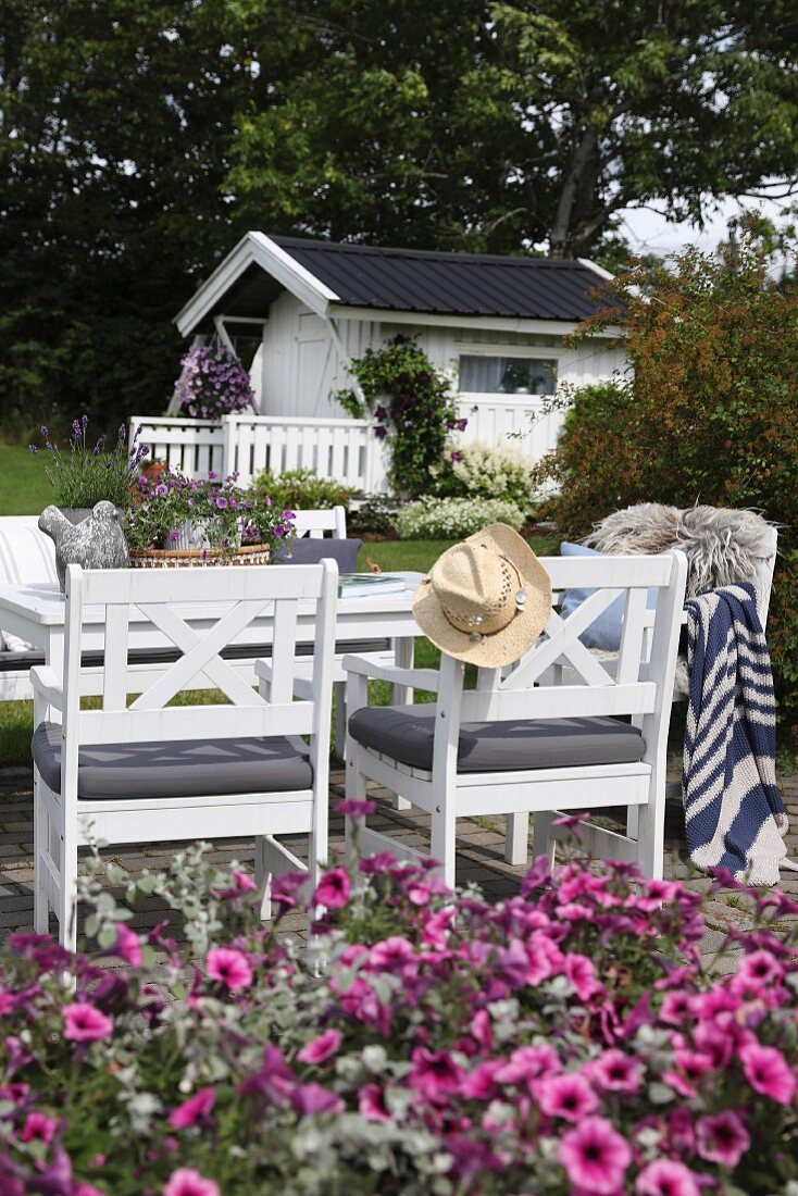 weiße Holzstühle und Tisch auf Terrasse, im Hintergrund Gartenhäuschen