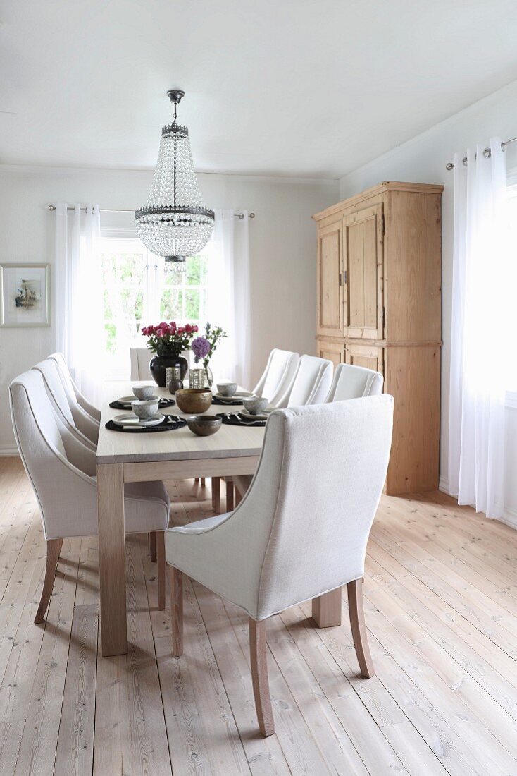 Chairs with pale upholstery around dining table below chandelier