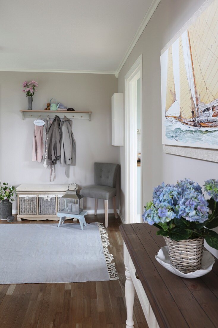 Entrance area with wall-mounted coat rack, trunk and potted blue hydrangea on console table in foreground