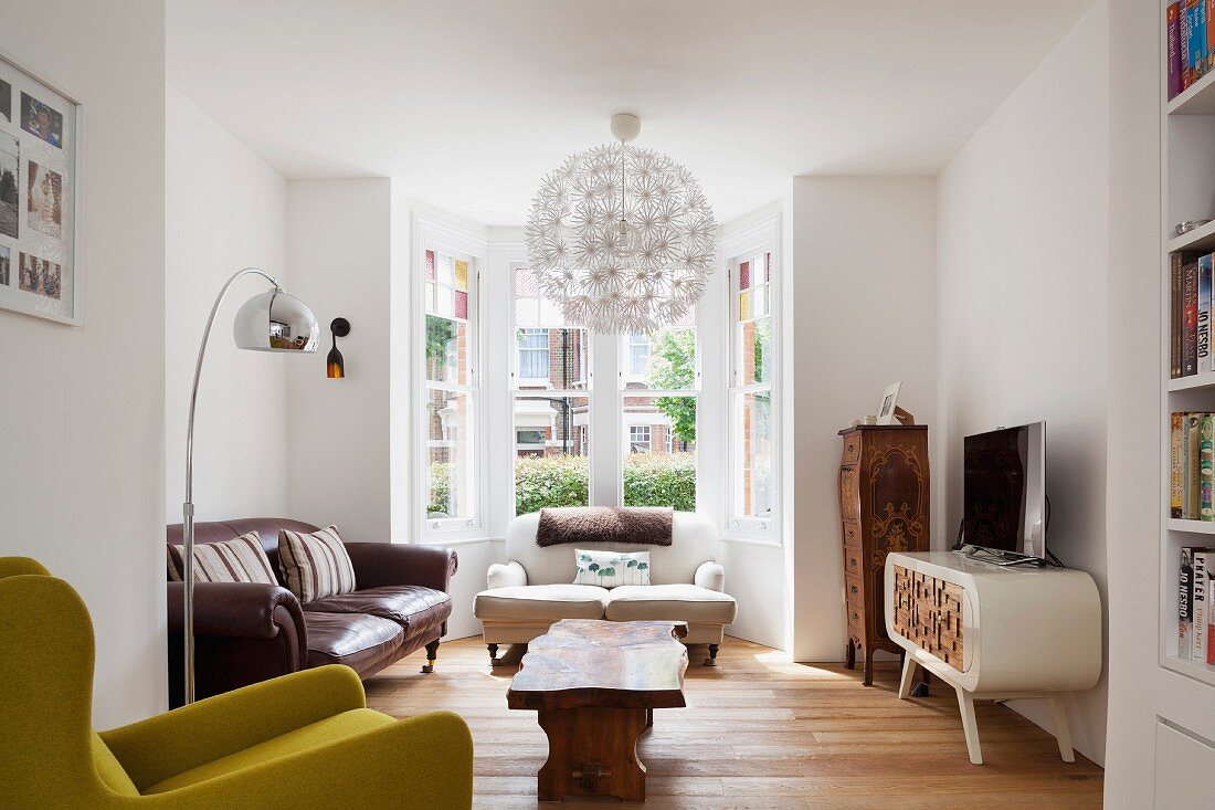 Bay window, spherical pendant lamp, wooden coffee table and antique sofas in eclectic interior