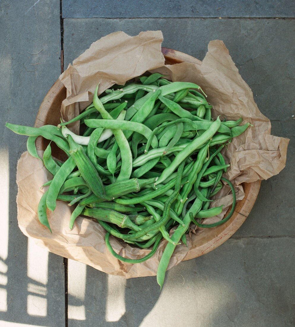 Green beans and okra pods on a piece of paper in a wooden bowl