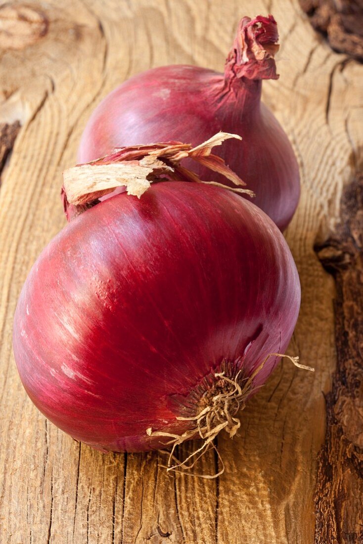 Two red onions on a wooden surface
