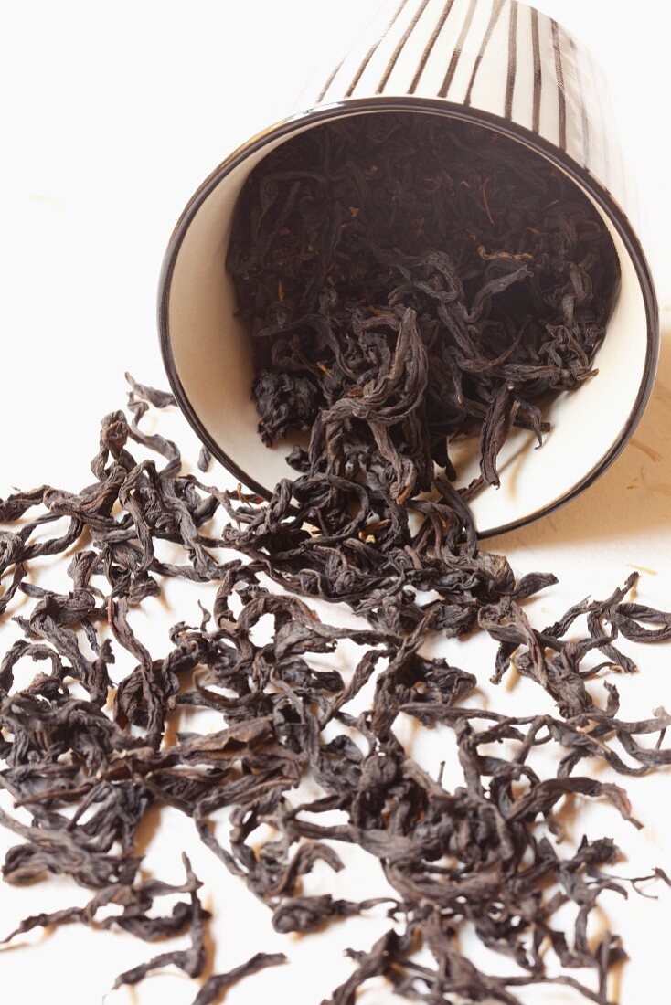 Umgekippter Becher mit schwarzen Teeblättern