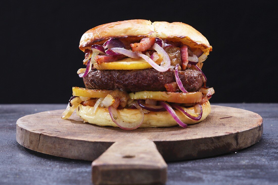 A burger with onions, bacon and apples on a wooden board