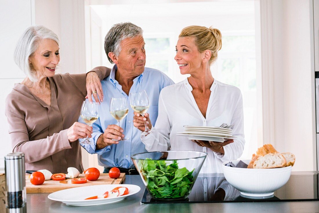 Kochen mit Freunden: Drei ältere Personen in der Küche stossen mit Wein an