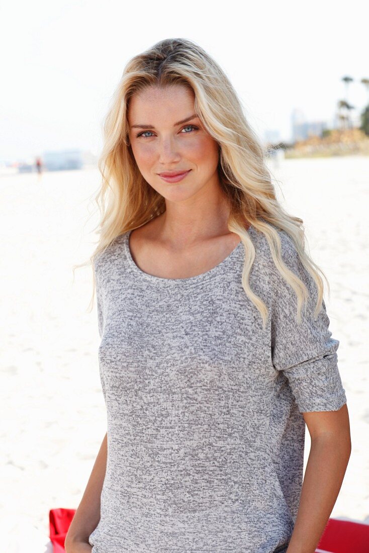 A young blonde woman wearing on a beach wearing a knitted mottled grey top
