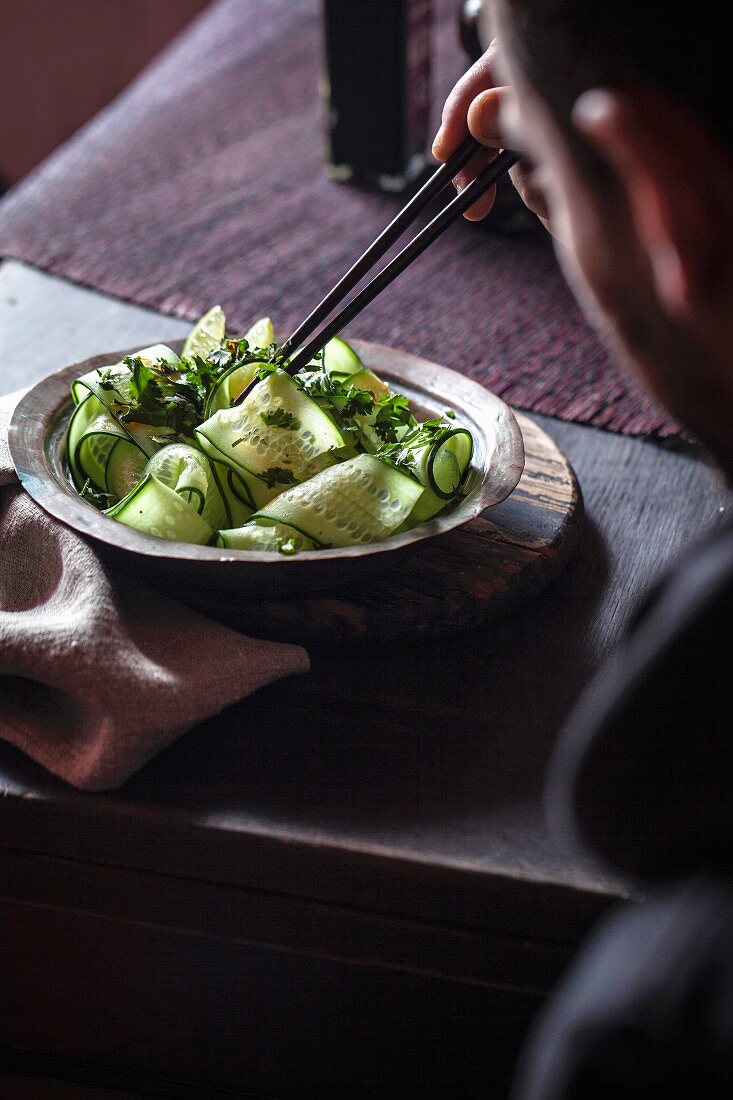 A man eating cucumber salad with chopsticks