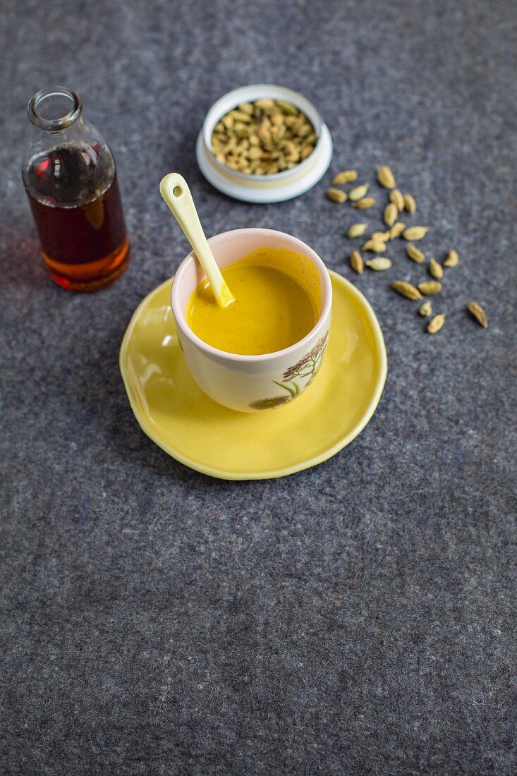 A cup of Vedic milk and a bottle of maple syrup with cardamom pods
