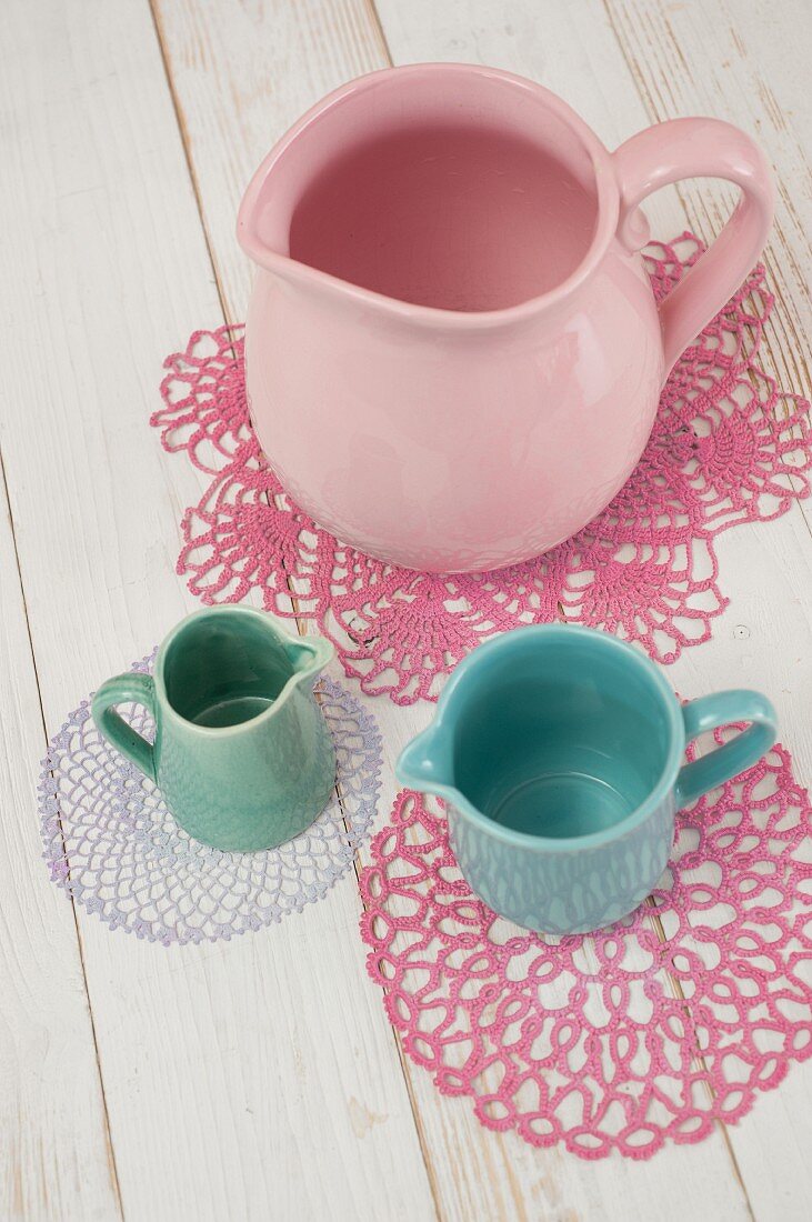 Various jugs on dyed lace doilies in pastel shades
