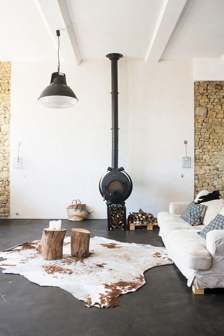 Cowhide rug on charcoal concrete floor and wood-burning stove in lounge area of loft apartment