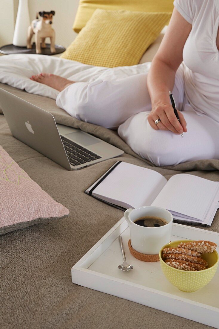 A woman with a breakfast tray working on a bed