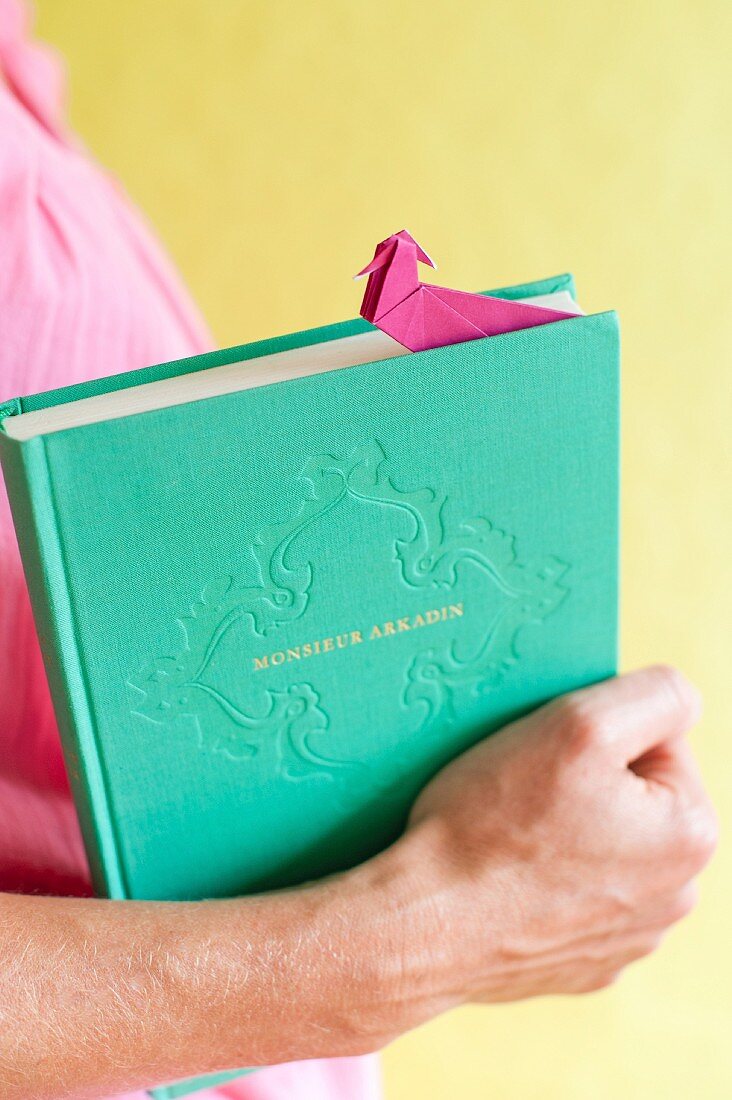 Hand hält Buch mit pinkfarbenem Origami-Lesezeichen
