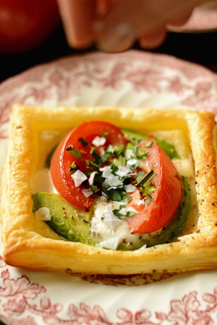 A puff pastry with baked egg, avocado and tomatoes being sprinkled with salt