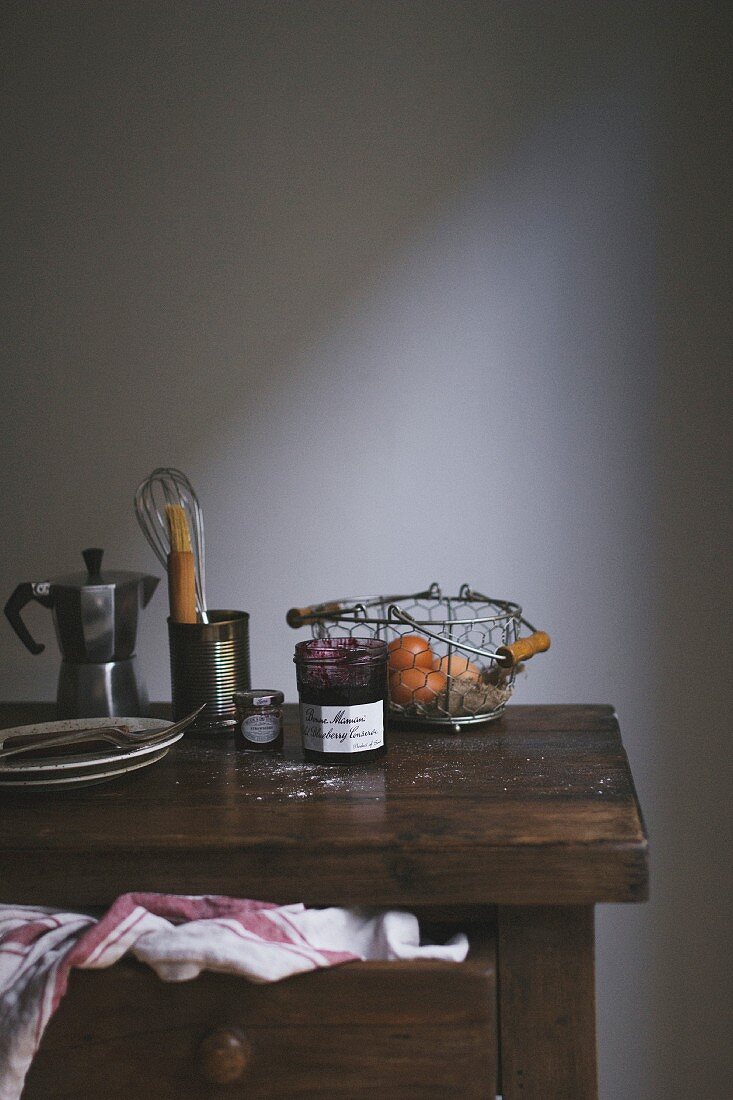 Jam, baking utensils, plates and an espresso machine on a wooden chest of drawers