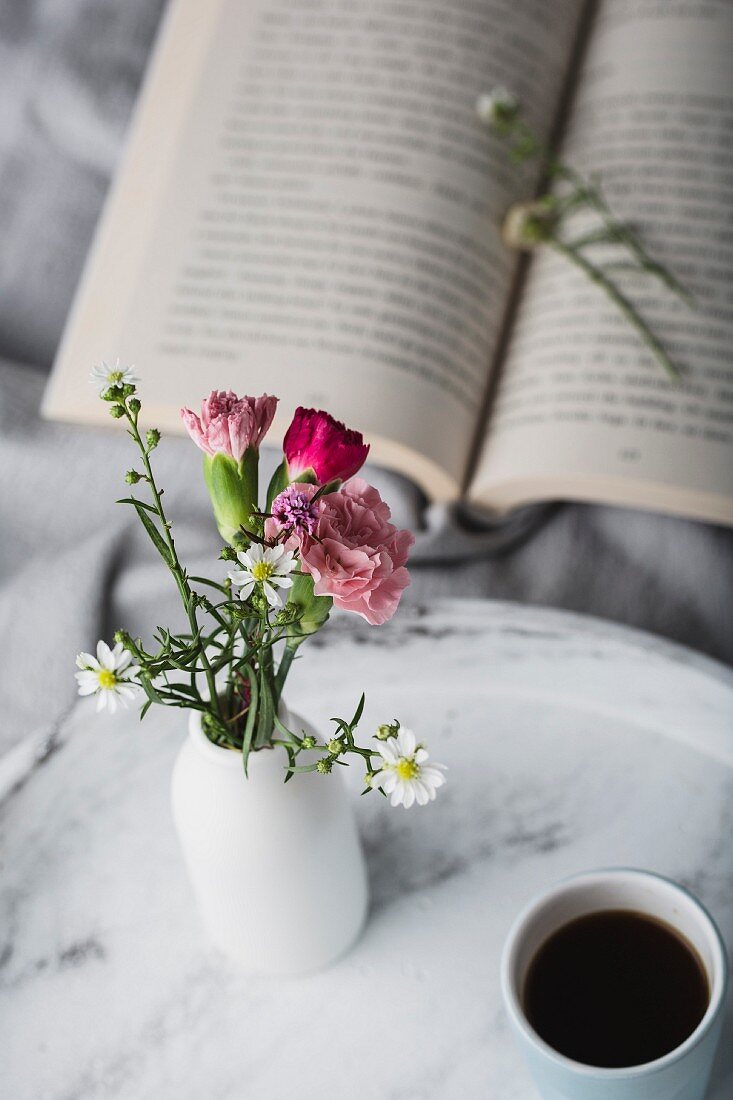Aufgeschlagenes Buch und Blumenvase mit Kaffeebecher auf Tablett im Bett