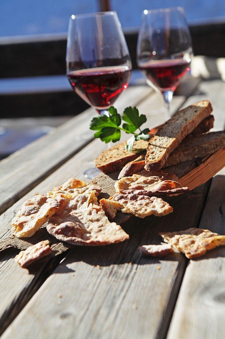 Schüttelbrot (crispy unleavened bread from South Tyrol) and Vinschgauer bread (rye-wheat sour dough) on a rustic wooden table with red wine