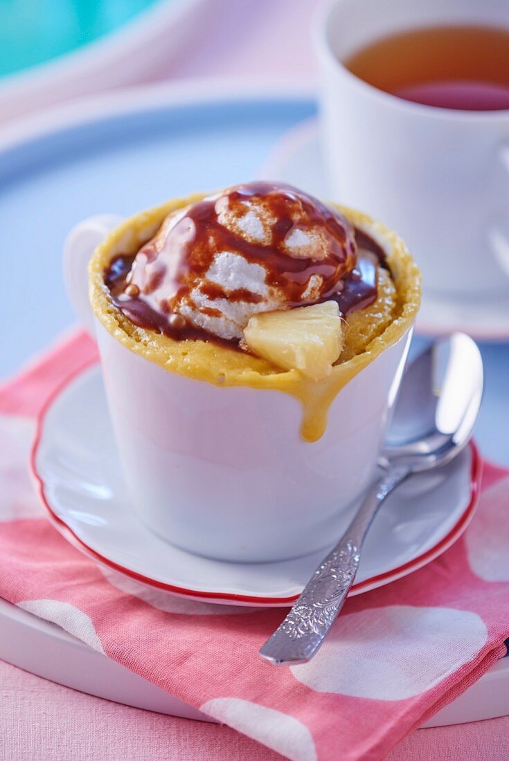 A mug cake with pineapple, a scoop of ice cream and chocolate sauce
