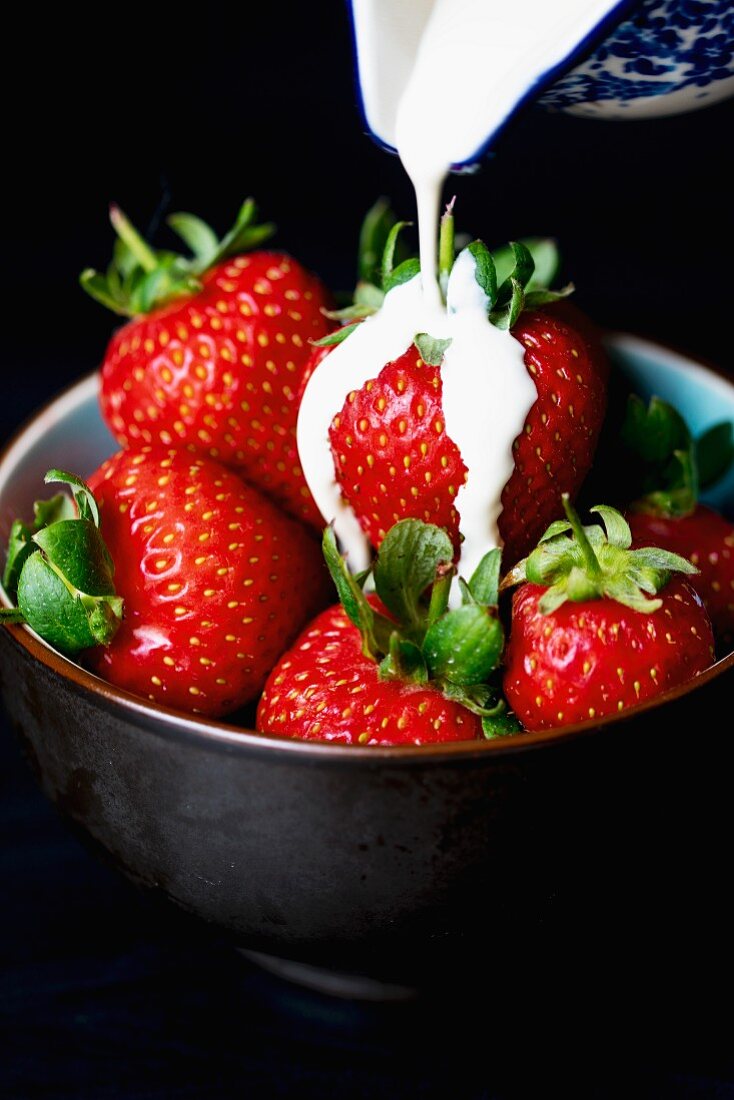 Cream being poured over a bowl of fresh strawberries