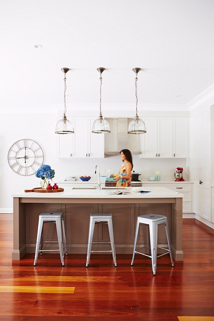 Kitchen island and retro bar stool under pendant lights, woman in front of white kitchen counter in background