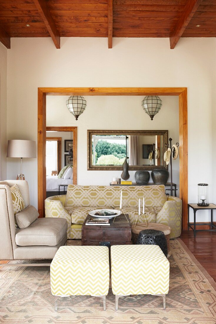 Polsterhocker, Sessel und Sofa im Wohnbereich mit Holzbalkendecke und breitem Wandausschnitt