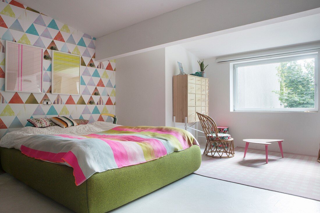 Colourful wallpaper on accent wall and green upholstered bed frame in bright bedroom