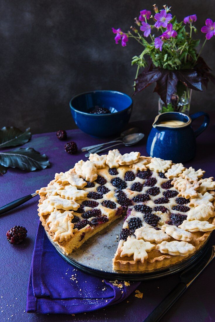 Mandel-Brombeer-Tarte, angeschnitten, und ein Krug Vanillesauce