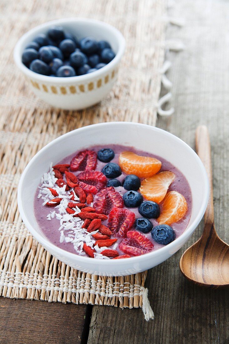 A bowl of smoothie with blueberries, desiccated coconut, goji berries, raspberries and clementines