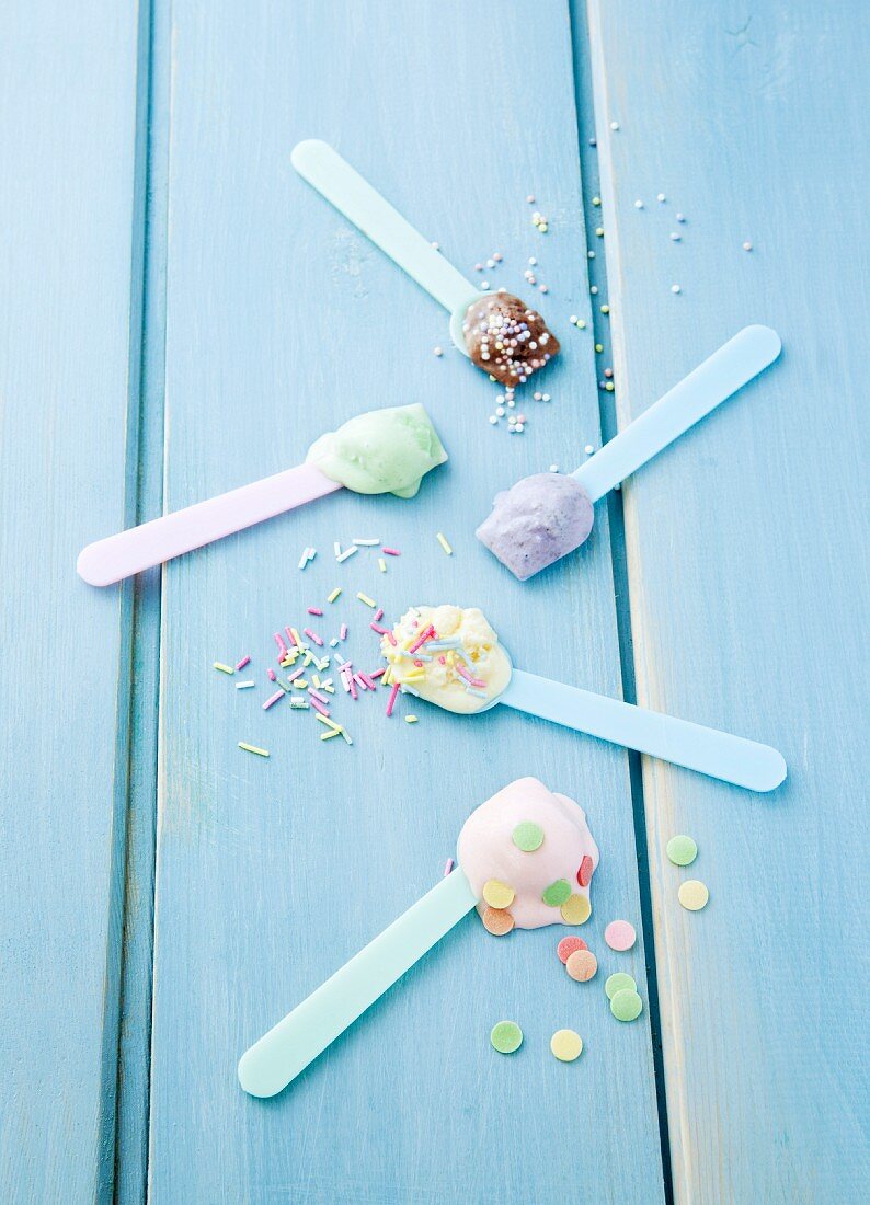 Various types of ice cream on ice cream spoons scattered with sugar sprinkles: vanilla, strawberry, chocolate, blueberry and mint