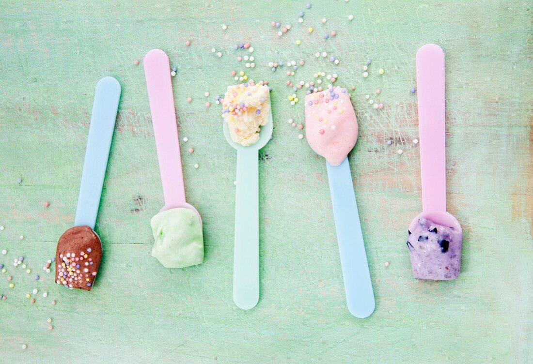 Various types of ice creams on ice cream spoons scattered with sugar pearls: vanilla, strawberry, chocolate, blueberry and mint