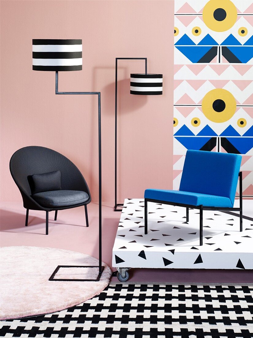 Black armchair, designer standard lamp, blue chair on platform against wallpaper and mixture of patterns