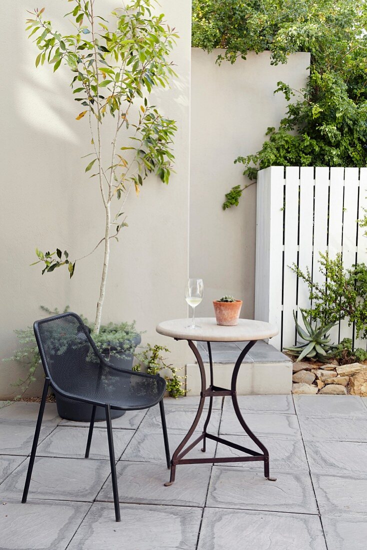 Schwarzer Drahtgeflechtstuhl und runder Gartentisch auf Terrasse