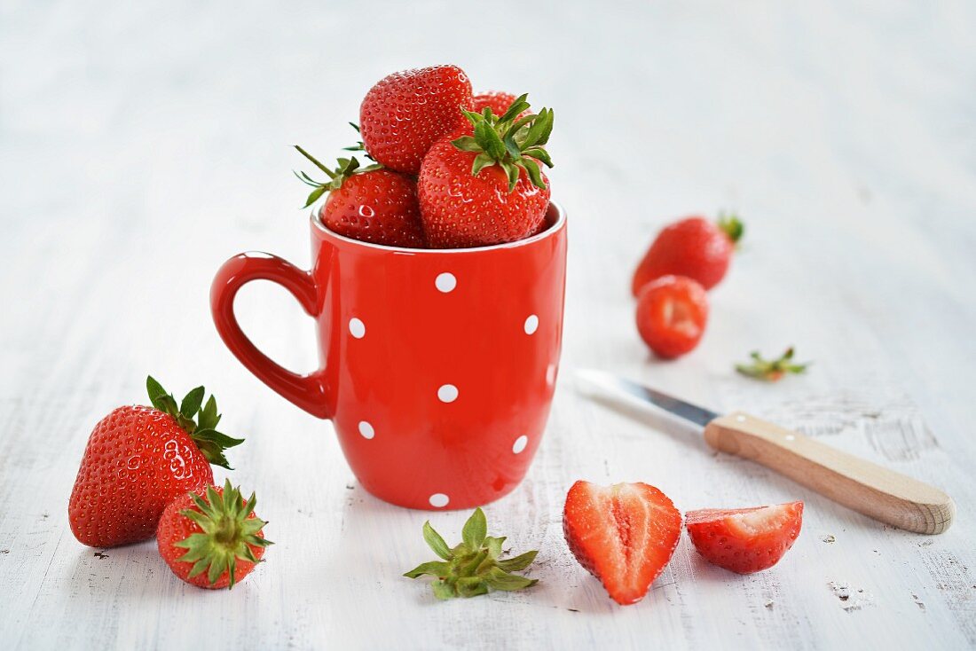Frische Erdbeeren in einer Tasse, daneben durchgeschnittene Früchte