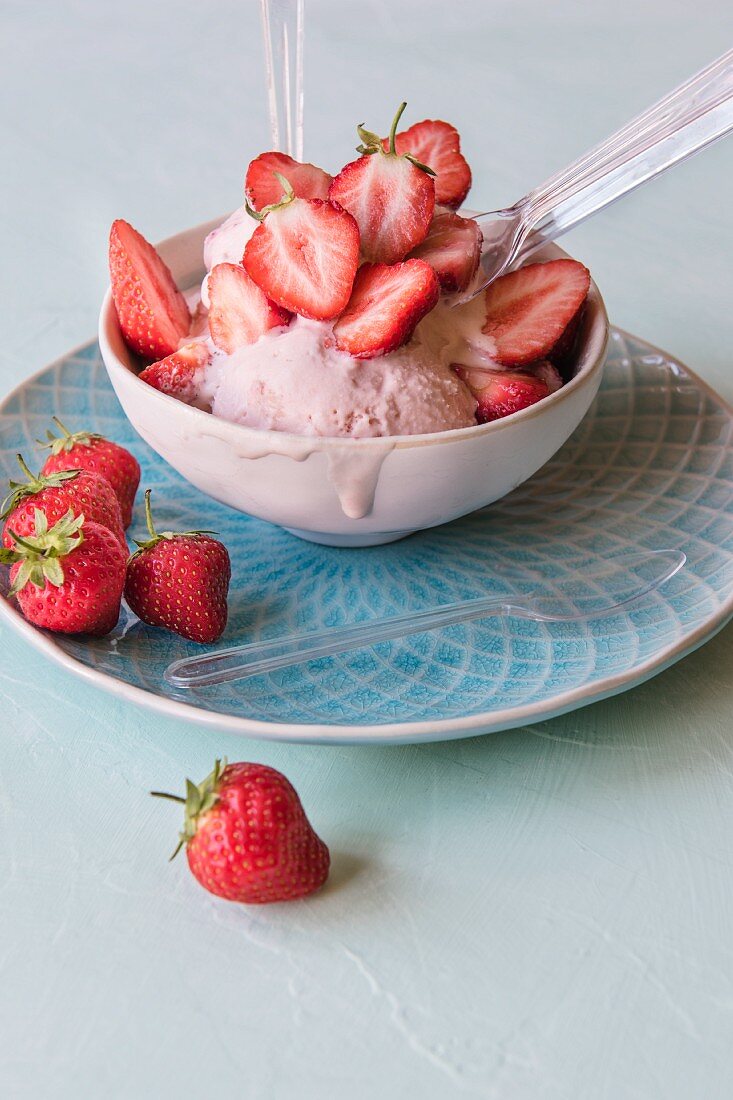 A bowl of strawberry ice cream with fresh strawberries.