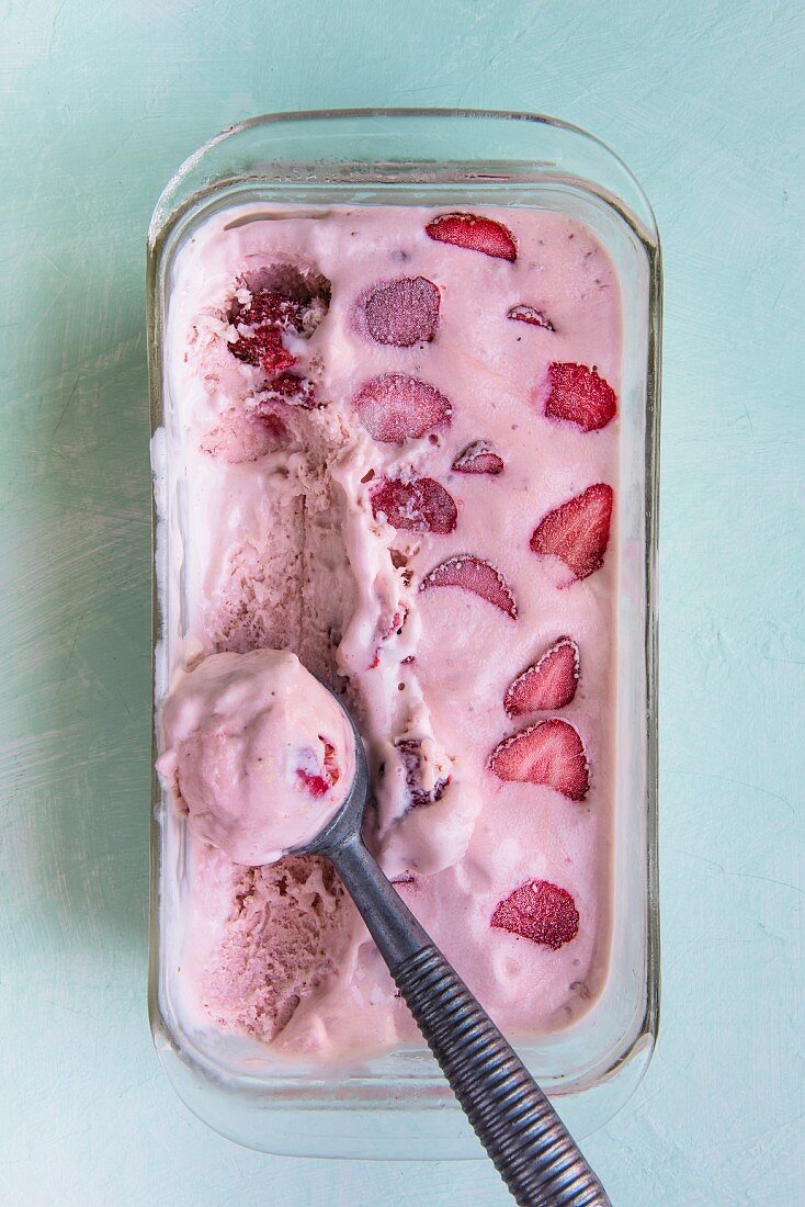 Homemade strawberry ice cream with an ice cream scoop in a glass dish (seen from above)