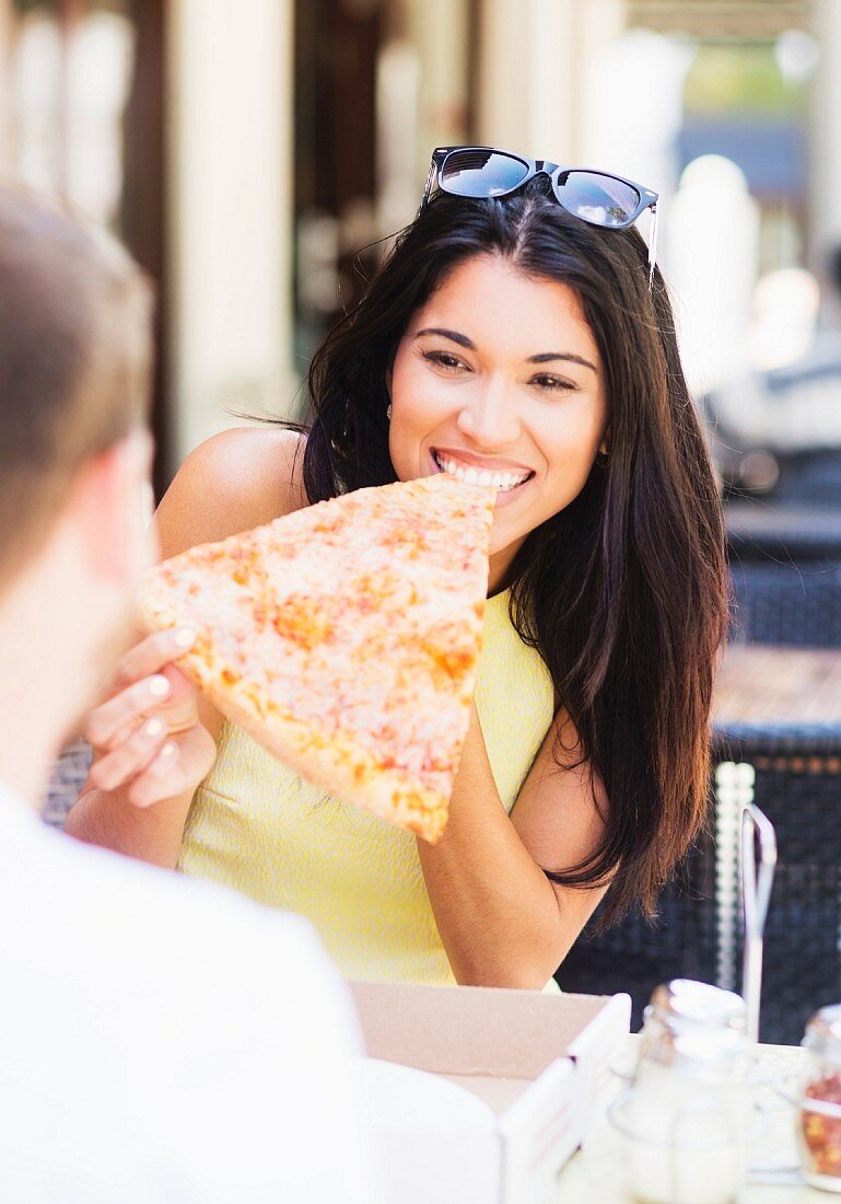 A woman eating a slice of pizza at a pavement cafe