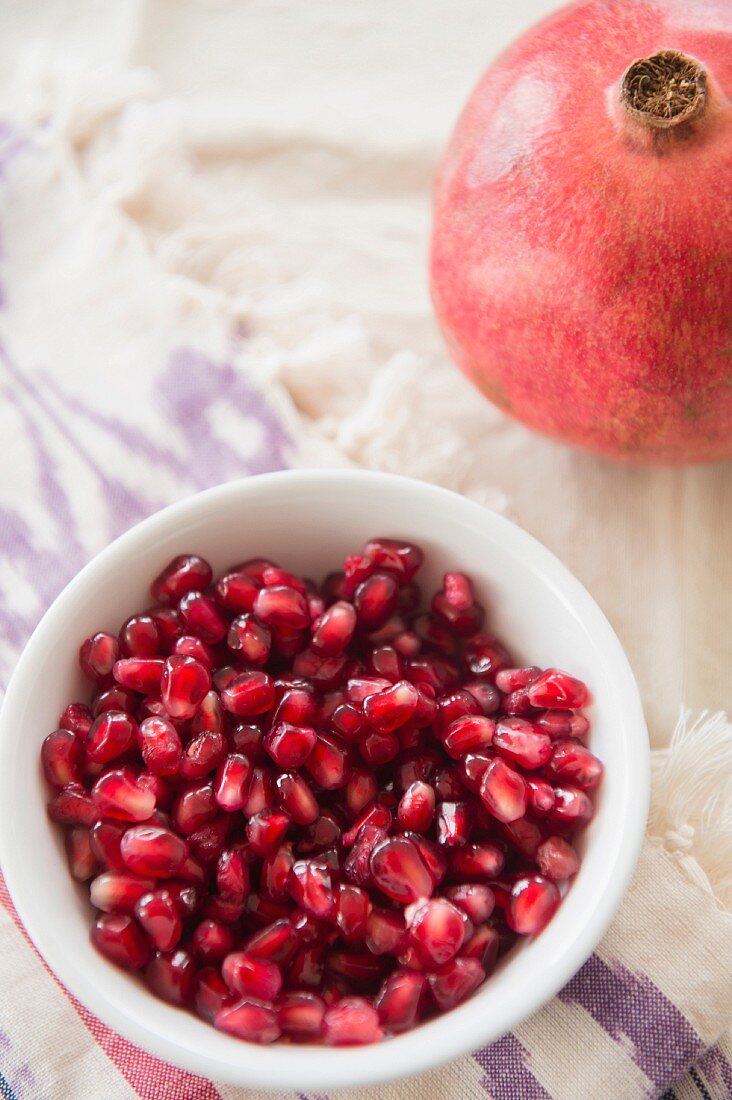 A whole pomegranate and a bowl of pomegranate seeds